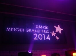Oplyst lilla skilt med Dansk Melodi Grand Prix 2014 med dekorative stjerner på mørk baggrund.