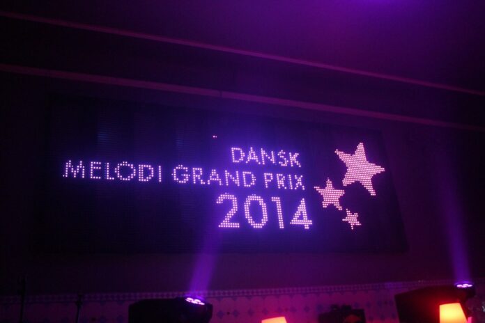Oplyst lilla skilt med Dansk Melodi Grand Prix 2014 med dekorative stjerner på mørk baggrund.